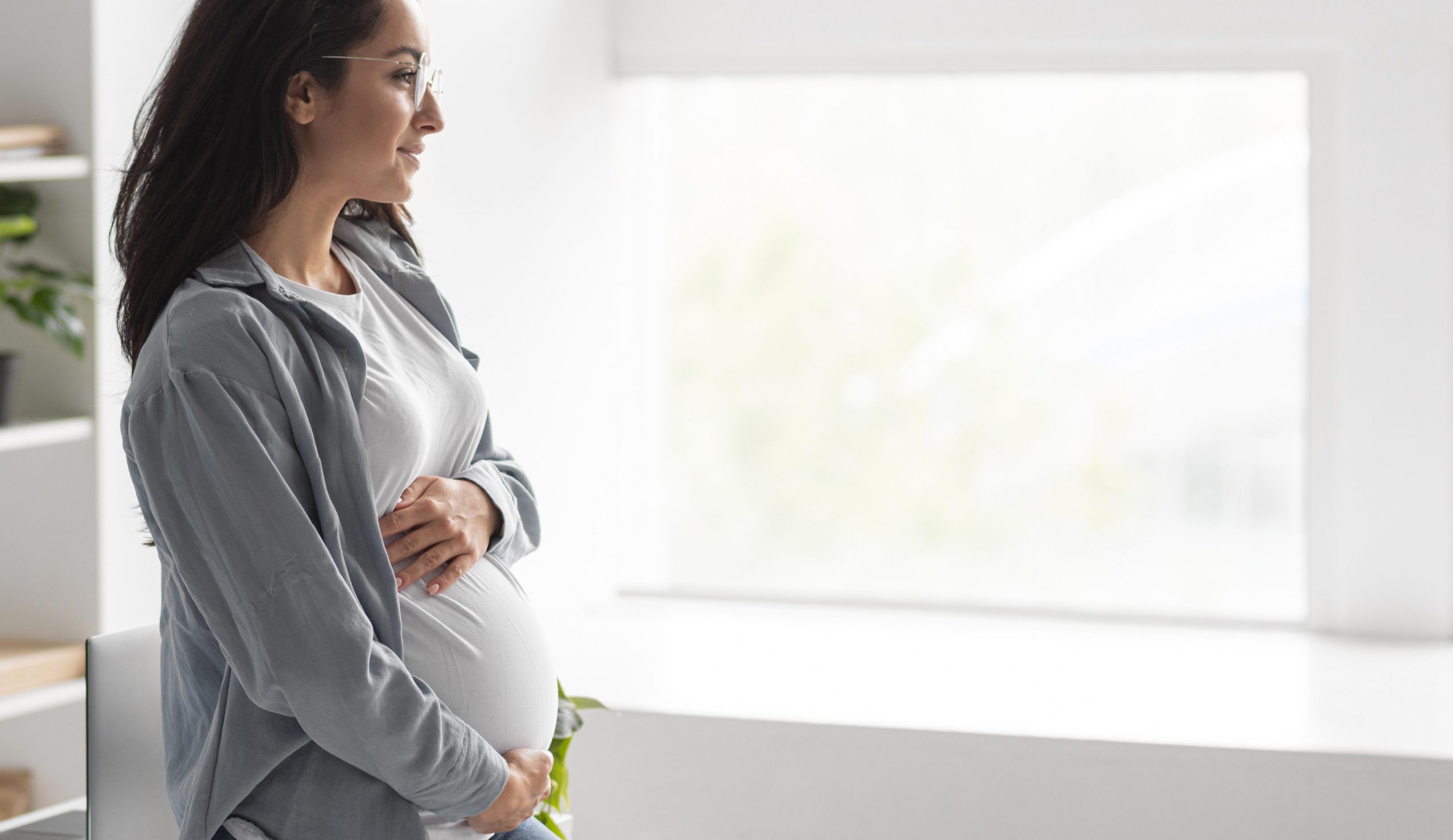 side-view-pregnant-woman-holding-her-belly-home-with-copy-space